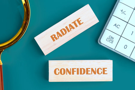 Words RADIATE CONFIDENCE made of wooden blocks on a green background next to a calculator, top view.