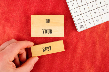 Business motivational concept. Copy space. Words BE YOUR BEST assembled from blocks in a composition with part of a white calculator and a hand, top view.の写真素材