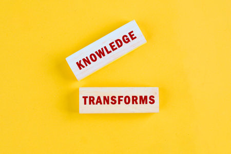 KNOWLEDGE TRANSFORMS concept words assembled from blocks on yellow background, top view.
