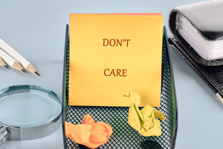 A notepad with dont care sits atop a wire mesh container holding crumpled paper near pencils and a...