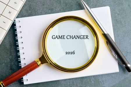 A magnifying glass focuses on the words GAME CHANGER 2026 on a notepad, positioned next to a pen and...