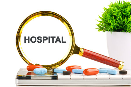 Close-up features a magnifying glass over the word Hospital. Pills scatter on a keyboard and a vibrant green plant sits nearby, bringing life to the concept of medical care.の写真素材