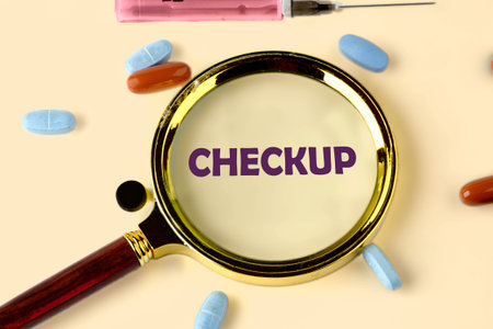 Pills, a syringe, and the word CHECKUP are seen through a magnifying glass. It represents the importance of health and preventative medicine through annual physicals.の写真素材