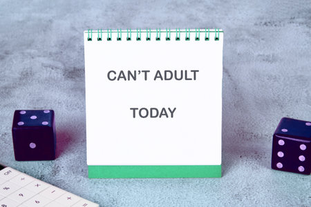 A white spiral notepad shows the words CANT ADULT TODAY, alongside dice and a calculator on a gray...