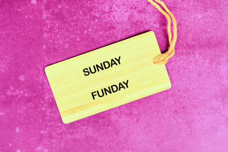 A light yellow tag with SUNDAY FUNDAY on it rests on a textured magenta surface, held by a string, implying a day full of laughter and good times is coming.の写真素材