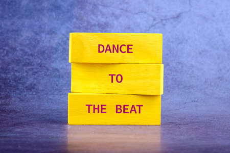 Three yellow blocks are stacked with words written on them. The words are Dance To The Beat. They stand against a mottled blue and gray background.の写真素材