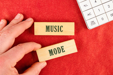 A hand positions carefully wooden blocks displaying the words MUSIC MODE on a bright red background,...