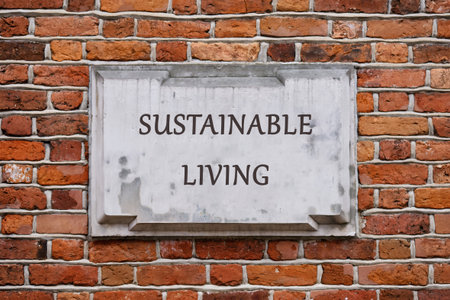 A rectangular stone plaque, bearing the inscription SUSTAINABLE LIVING, is affixed to a textured, red brick wall, suggesting an eco friendly environment.の写真素材