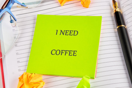 A vibrant green note boldly declares I NEED COFFEE, lying on a planner next to a pen and glasses. A...