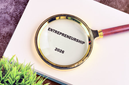 A magnifying glass with a wooden handle rests on a book, highlighting the word Entrepreneurship and...