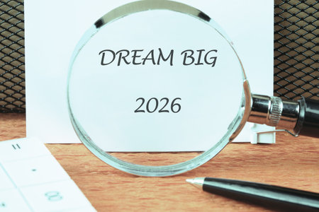 The words DREAM BIG and 2026 are visible through a magnifying glass on a white paper. A pen and...