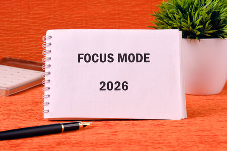 A note announces Focus Mode for 2026. A pen rests nearby, along with a notepad and small plant, all sitting on a textured orange surface.の写真素材