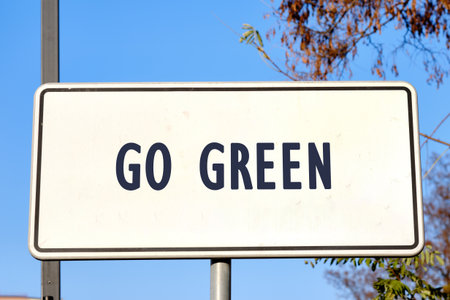 A sign, against a bright blue sky and foliage, displays the words GO GREEN, a call to action to embrace eco-friendly practices for a healthier planet.の写真素材