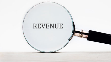 A magnifying glass hovers above the word revenue, emphasizing its importance and inviting viewers to examine financial concepts more closely in a clear and simplistic manner.の写真素材