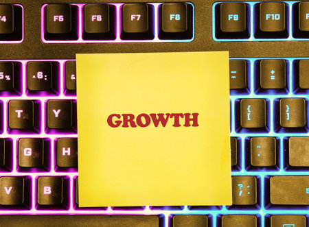 A bright yellow sticky note with the word growth stands out on a colorful keyboard. The scene captures a moment of inspiration, creativity, and motivation in a workspace.の写真素材