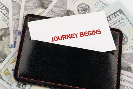 A sleek black wallet holds a card that says journey begins, surrounded by crisp hundred dollar...