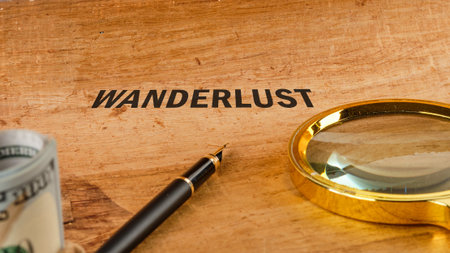 A wooden table displays the word wanderlust alongside a magnifying glass, a pen, and rolled currency, symbolizing the desire for travel and discovery in life.の写真素材