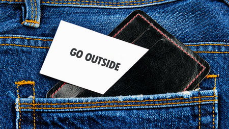 A card with the message to go outside is placed neatly in the back pocket of a pair of blue jeans. This scene invites spontaneity and outdoor fun at any time.の写真素材