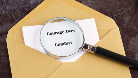 An envelope rests on a textured surface, revealing a message that reads Courage Over Comfort.