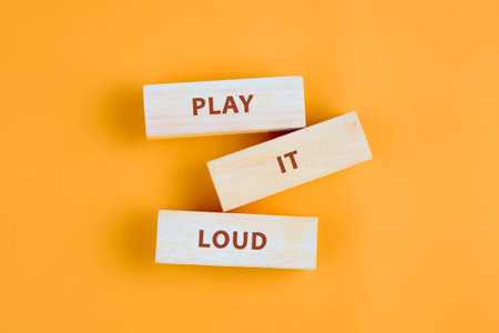 Three wooden blocks arranged artistically display the motivational phrase play it loud, set against a warm orange backdrop that radiates positivity, perfect for energizing any space.の写真素材