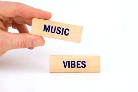 A hand holds two wooden blocks, each displaying the words MUSIC and VIBES in bold blue letters. This artistic representation captures the essence of creativity and joy through sound.の写真素材