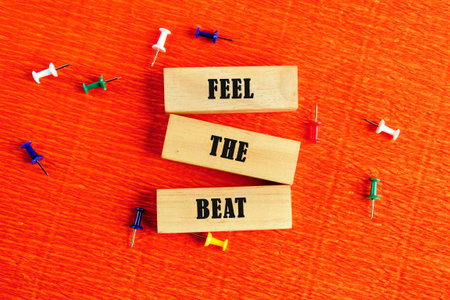 Wooden blocks arrange the words Feel the Beat scattered among colorful pins on a bright orange...
