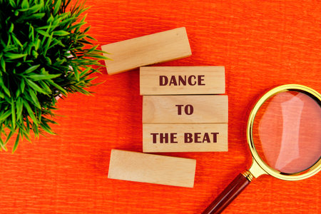 Colorful wooden blocks spell out a fun phrase about dancing. A magnifying glass adds interest. Green plant brings life to the bright orange surface, creating a lively scene.の写真素材
