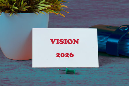 A card displaying the title Vision 2026 sits on a rustic wooden table beside a small potted plant.の写真素材