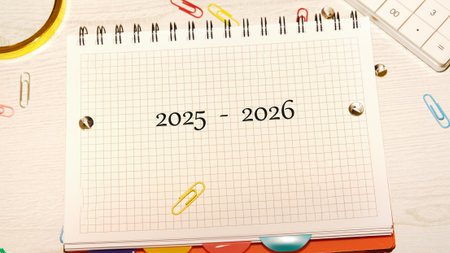 A grid notebook lays open, showing the years 2025 to 2026. Surrounded by vibrant paper clips and a...
