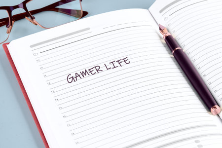 A cozy workspace features an open notebook with the words Gamer Life artfully written. A pen and a...