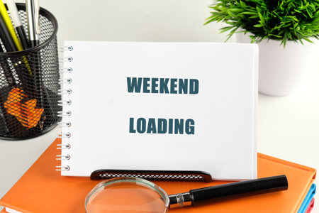 A sign reading weekend loading rests on an organized desk surrounded by stationery and a small green plant, evoking excitement for the approaching break and relaxation.の写真素材
