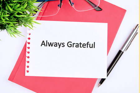 A bright workspace features a note that says always grateful, surrounded by a green plant, glasses, and a sleek pen, promoting positivity and mindfulness.の写真素材