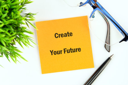A bright yellow sticky note placed on a clean surface features the phrase Create Your Future. Accompanying the note are stylish glasses and a sleek pen, promoting a positive mindset.の写真素材