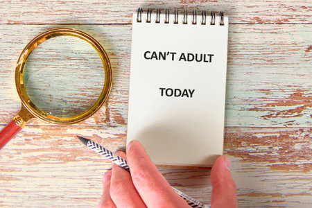 In a cozy workspace, a hand grasps a pencil next to a notepad stating cant adult today, surrounded by a magnifying glass, reflecting the desire for a stress-free day and relaxation.の写真素材