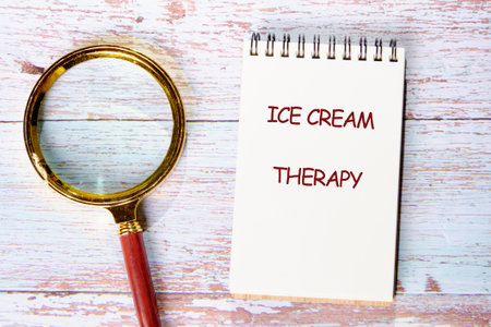 A notepad with the words ice cream therapy sits beside a magnifying glass on a rustic wooden table.の写真素材