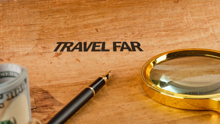 A wooden surface showcases the words Travel Far, accompanied by a magnifying glass and a pen, symbolizing adventures ahead. A hint of currency reflects the value of exploration.の写真素材