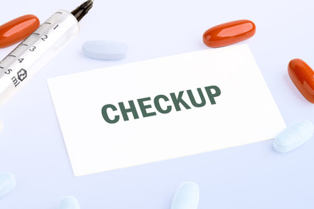 A clean surface showcases a syringe, colorful pills, and a card reading checkup. These items indicate preparation for a health assessment, promoting well-being and care.の写真素材