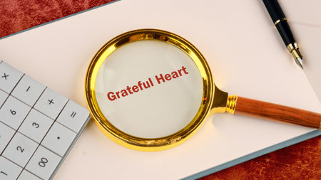 In a tranquil workspace, a magnifying glass rests on a notepad, highlighting the words Grateful Heart. A calculator and pen nearby suggest thoughtful planning and introspection.の写真素材