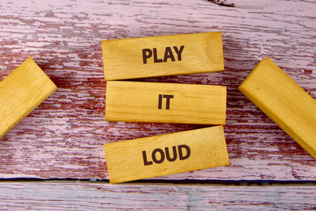 Wooden blocks with bold letters spell out a cheerful message about playing music loudly. The backdrop features rustic pink wood, creating an inviting and playful atmosphere.の写真素材