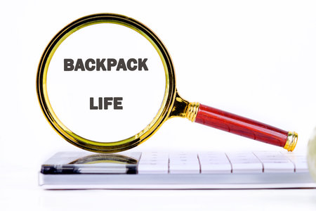 A magnifying glass focuses on the words backpack life, symbolizing exploration and discovery. It rests on a sleek notebook, reflecting a balance of adventure and organization.の写真素材