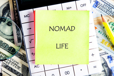 A bright sticky note featuring the words nomad life stands out against a background of a calculator, money, and a magnifying glass, symbolizing financial journeys and exploration.の写真素材