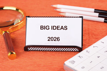 A workspace featuring a sign that reads big ideas 2026, a magnifying glass, and writing tools. It...