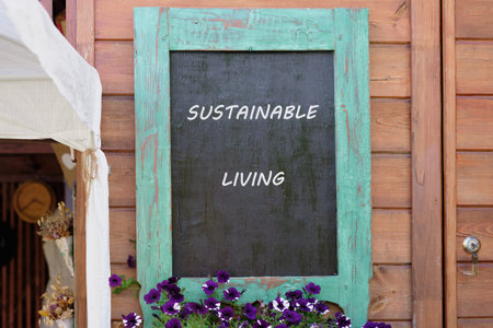 In a charming outdoor space, a wooden sign features the words sustainable living, surrounded by blooming purple flowers that enhance the warm atmosphere of the area.の写真素材