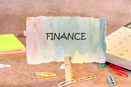 A vibrant card labeled finance stands upright on a desk surrounded by colorful paper clips, sticky notes, and a calculator, symbolizing financial planning and organization.の写真素材