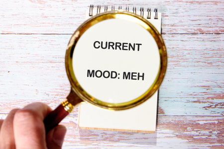 Person holds a magnifying glass over a spiral notepad. The notepad displays the phrase CURRENT MOOD...