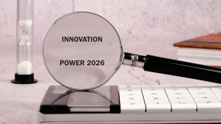 A magnifying glass focuses on the words INNOVATION POWER 2026. An hourglass stands nearby as do books. A calculator sits beneath the glass on a desk.の写真素材