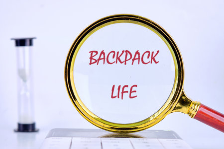 A golden magnifying glass highlights the phrase BACKPACK LIFE on a white surfaceの写真素材