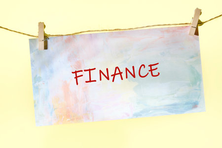 A vibrant piece of paper with the word finance written boldly in red is attached to a line by clothespins.の写真素材