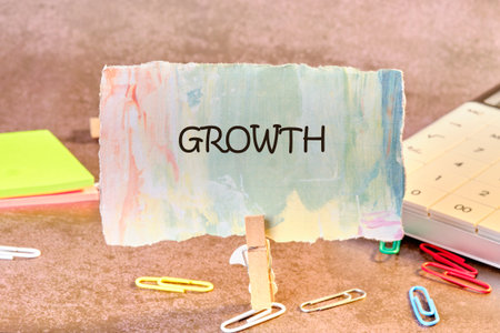 A vibrant piece of paper labeled Growth stands upright, surrounded by colorful paper clips and sticky notes, with a calculator nearby, capturing a moment of inspiration in a workspace.の写真素材