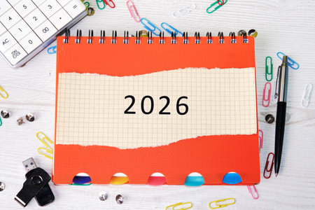 A bright orange calendar marked with 2026 stands out among colorful paper clips, a pen, and other...